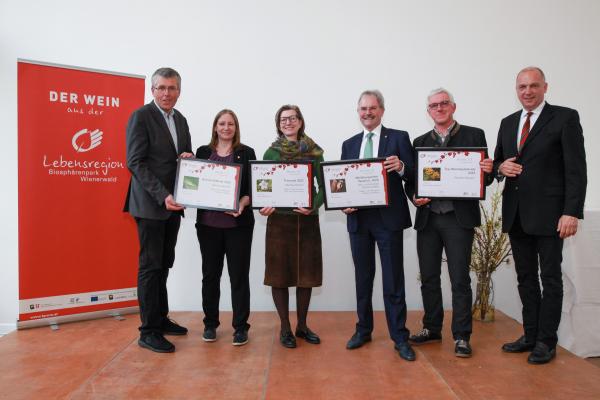 NÖ LAbg. Martin Schuster, Wiener LAbg. Mag.a Nina Abrahamczik (1. und 2.v.li), NÖ Landtagspräsident Mag. Karl Wilfing, Biosphärenpark-Direktor DI Andreas Weiß und Bezirkshauptmann von Mödling Dr. Philipp Enzinger (alle drei rechts außen) gratulieren den PreisträgerInnen aus dem Raum Mödling (Mitte): Weinbau Barbach zum Sieg in der Kategorie Perl- und Schaumwein und Weißwein Klassik und zum Top-Weinbaubetrieb und Wein und Heuriger Pferschy-Seper zum Sieg in der Kategorie Weißwein Reserve (nicht im Bild).