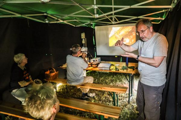 Menschen in dunklen Zelt mit Mikroskopbildern auf einer Leinwand