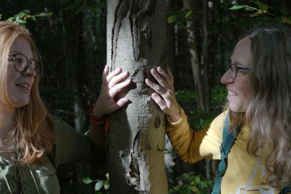 Zwei Frauen legen ihre Hände auf einen Baum und sehen sich an