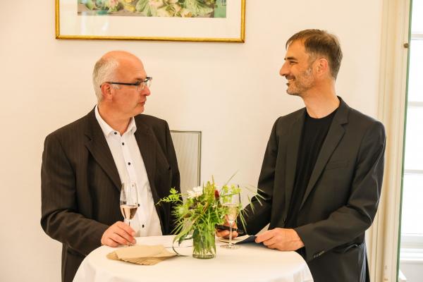 zwei Herren unterhalten sich bei einem Tisch mit Blumendeko