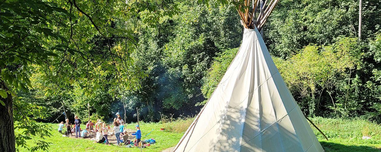 Tipi mit spielenden Kindern auf Waldlichtung