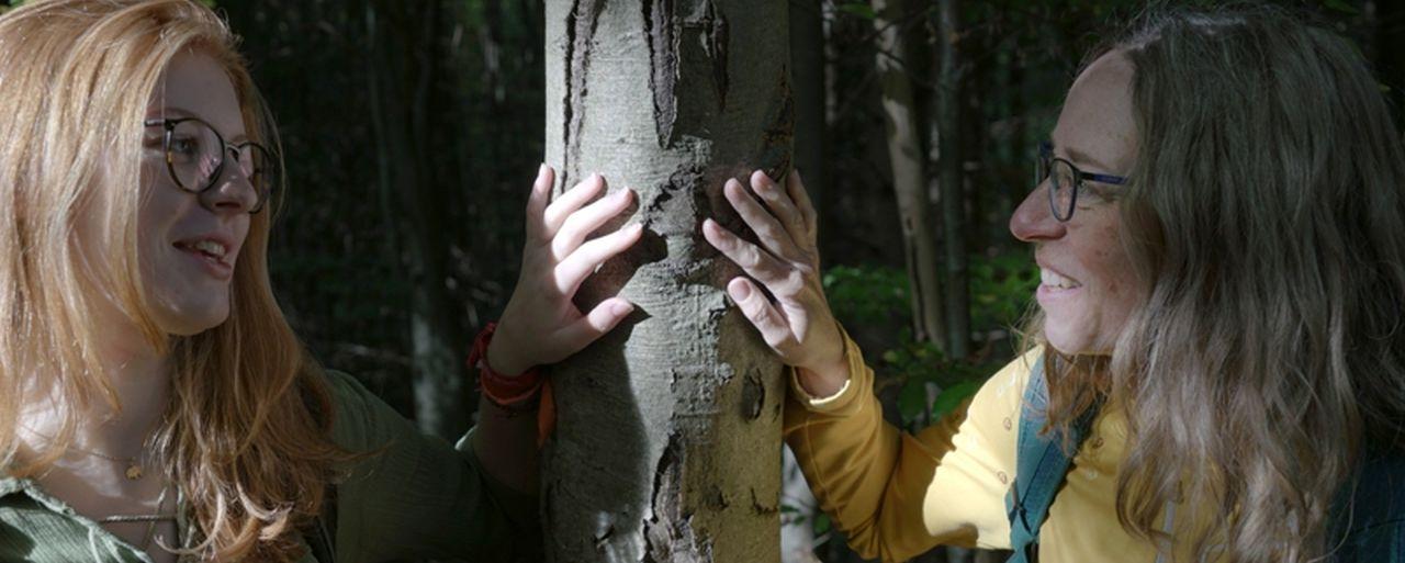 zwei Frauen halten ihre Hände auf einen Baum und sehen sich an