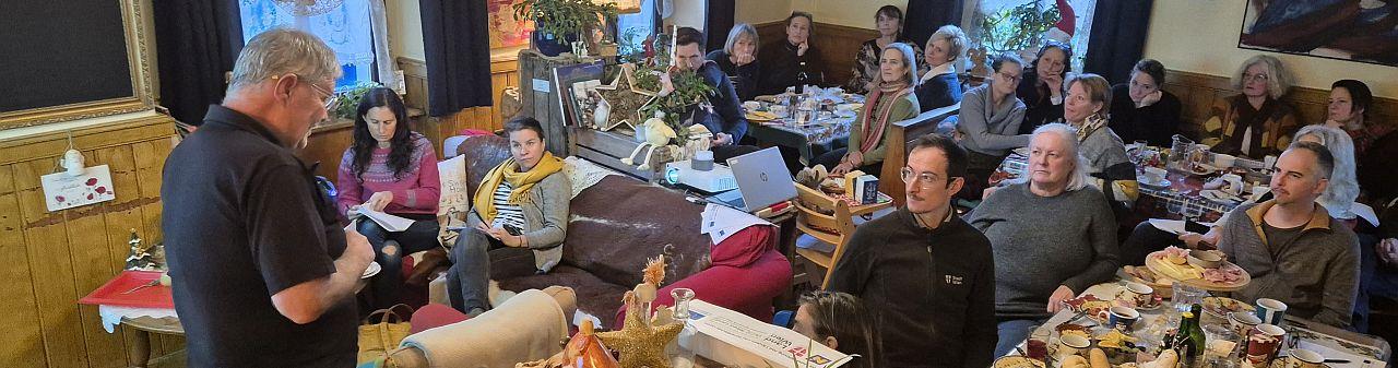 Personen sitzen rund um Tische und hören einen Vortrag