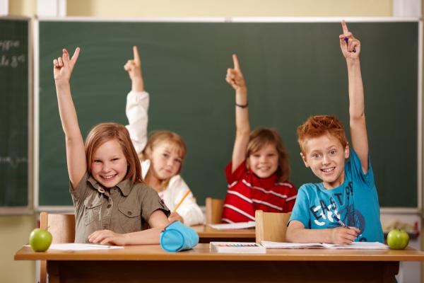 Kinder in einer Schulklasse zeigen auf