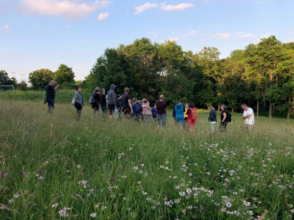 Menschen stehen in hohem Gras in einem Feld, umgeben von grüner Natur.