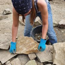 Kursteilnehmerin legt einen großen Stein auf die Trockensteinmauer