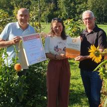 Bürgermeister Michael Krischke, Sonja Broser, BP-Direktor Andreas Weiß mit Urkunde im Blumenfeld